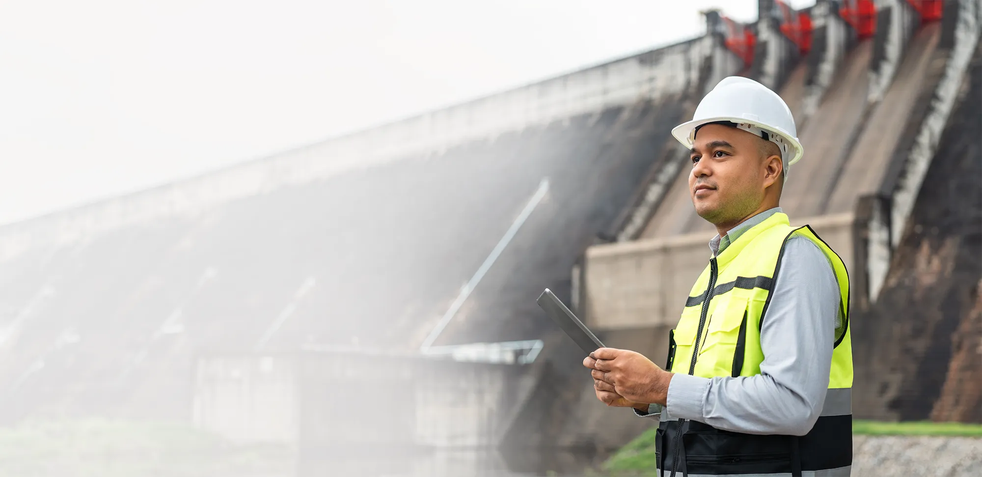 Water engineer standing next to a dam in high vis clothing and holding a tablet