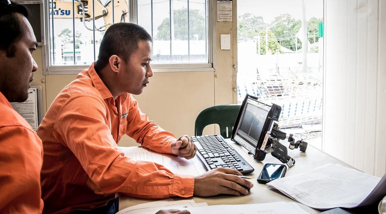 Man in high vis clothing sitting at a desk and looking at a laptop screen